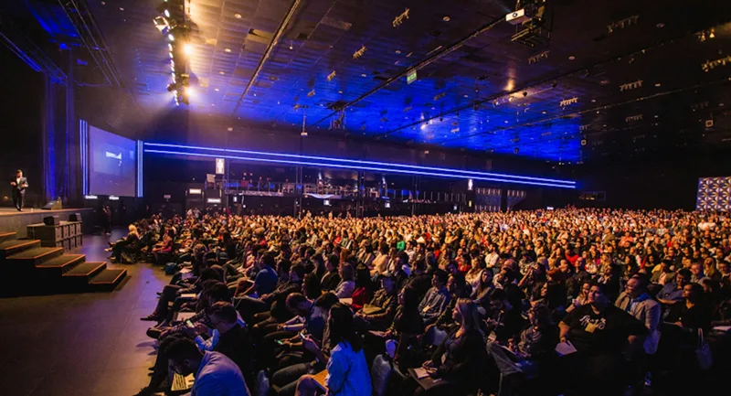 Audience and speaker in a blue-lit conference auditorium