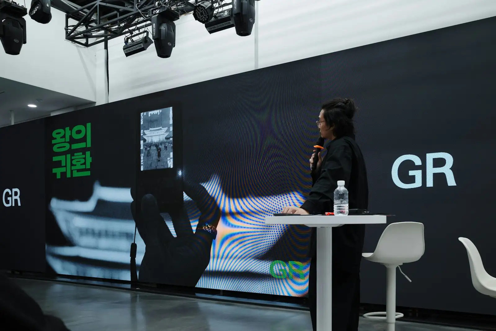 A person speaks at a presentation with a large screen