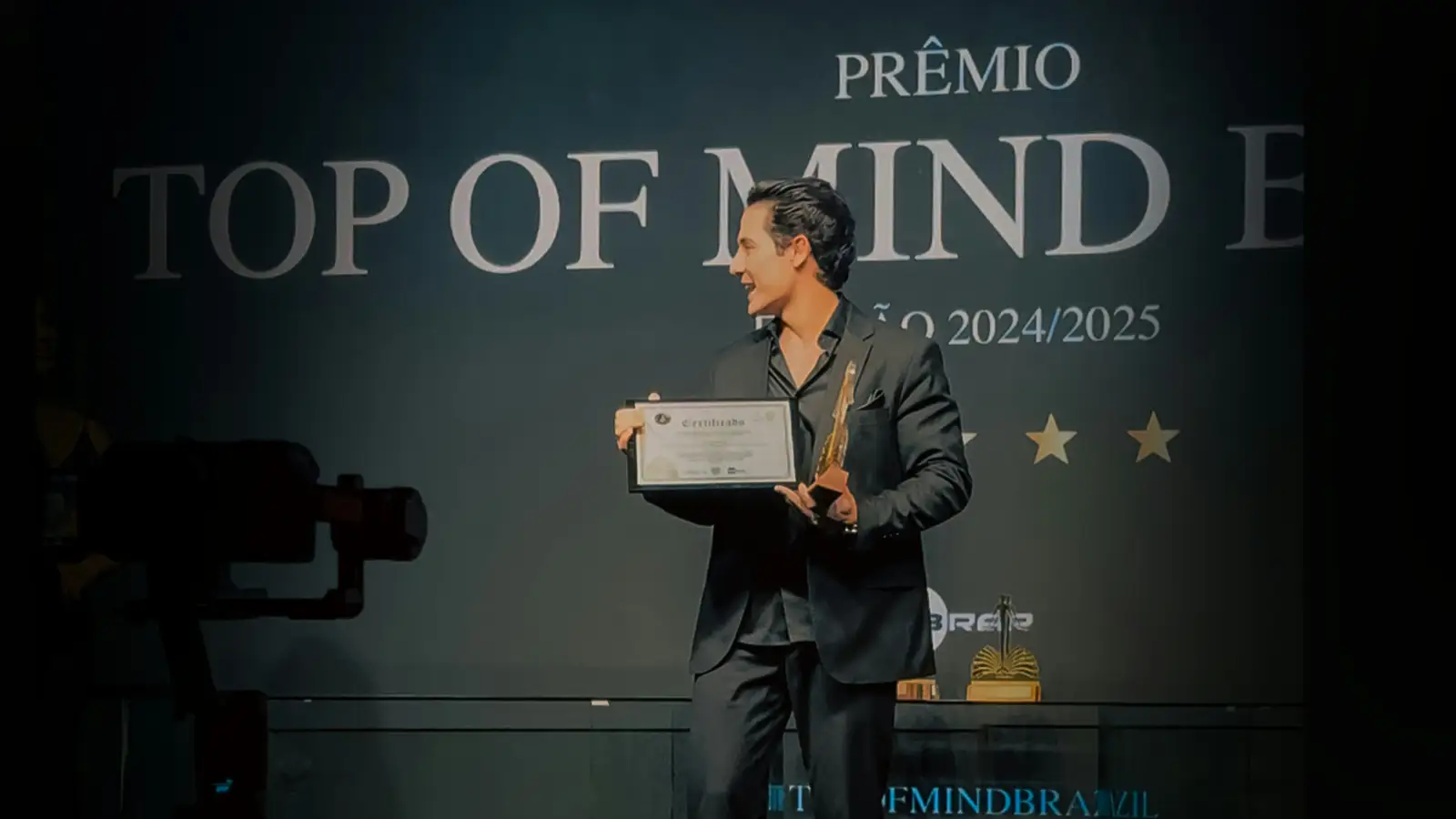 Award recipient holding a trophy in front of a branded ceremony backdrop