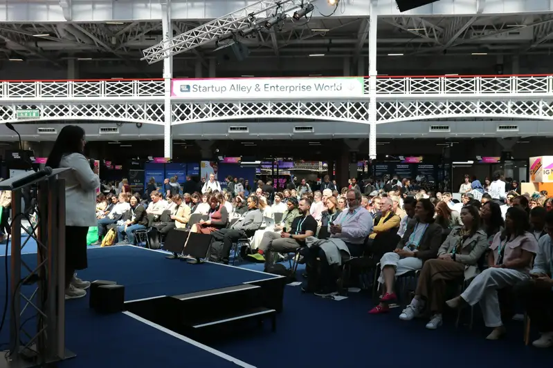 A speaker addresses an audience at an indoor conference event